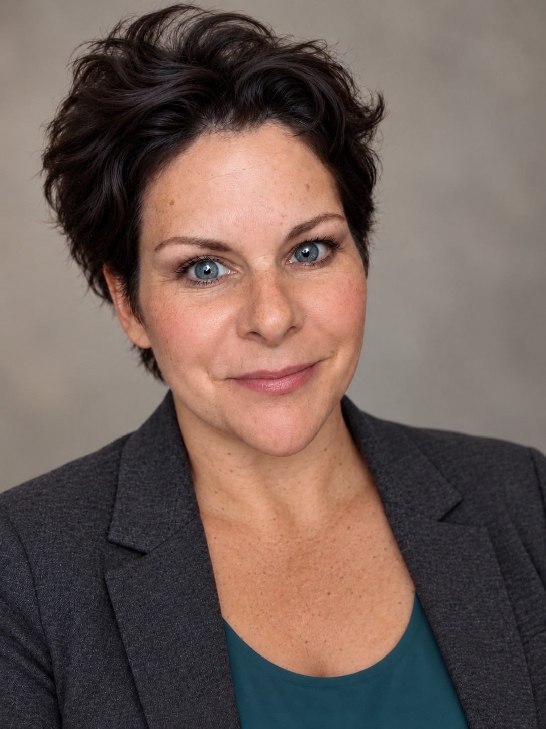 Lyd O’Grady, with short dark hair, wearing a teal top and charcoal jacket